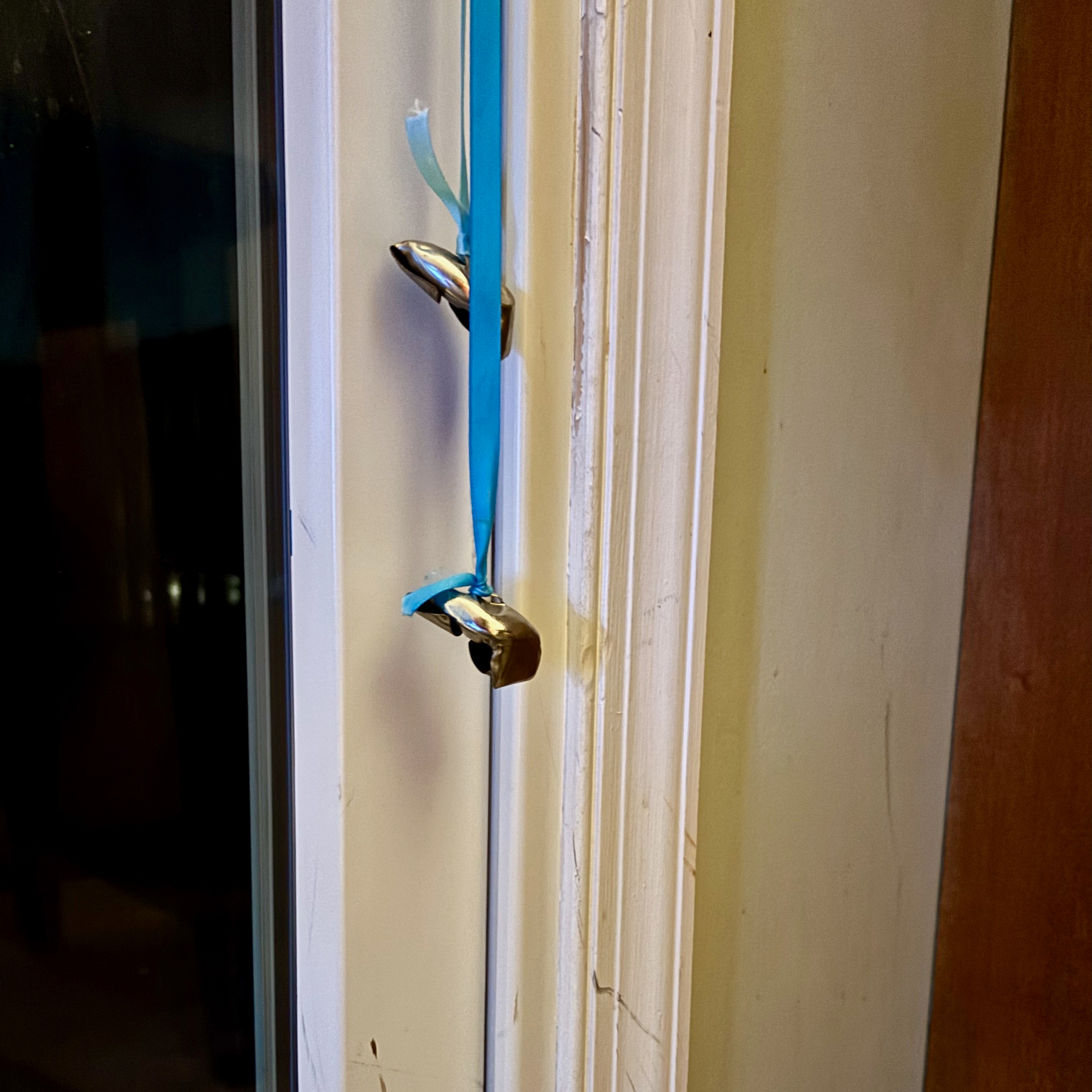 A blue ribbon is tied around the handles of a closed sliding glass door. Attached bells are smashed up.